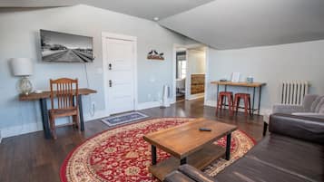 Un salon avec une table basse en bois, un tapis rouge à motifs, un canapé et un téléviseur fixé au mur.
