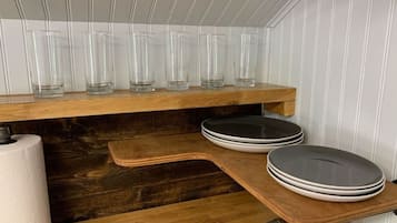 Et køkken med træhylder, der indeholder klare glas, en rulle køkkenrulle og stablede tallerkener.