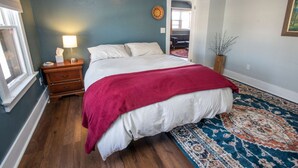 Une chambre à coucher avec un grand lit, une table de chevet, une lampe, un tapis et une porte donnant sur une autre pièce.