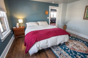 A bedroom with a large bed, a nightstand, a lamp, a rug, and a door leading to another room.