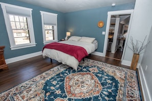 A bedroom with a bed, a nightstand, a lamp, and a large patterned rug.