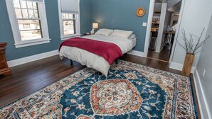 Un dormitorio con cama, mesita de noche, lámpara y una alfombra grande con estampado.