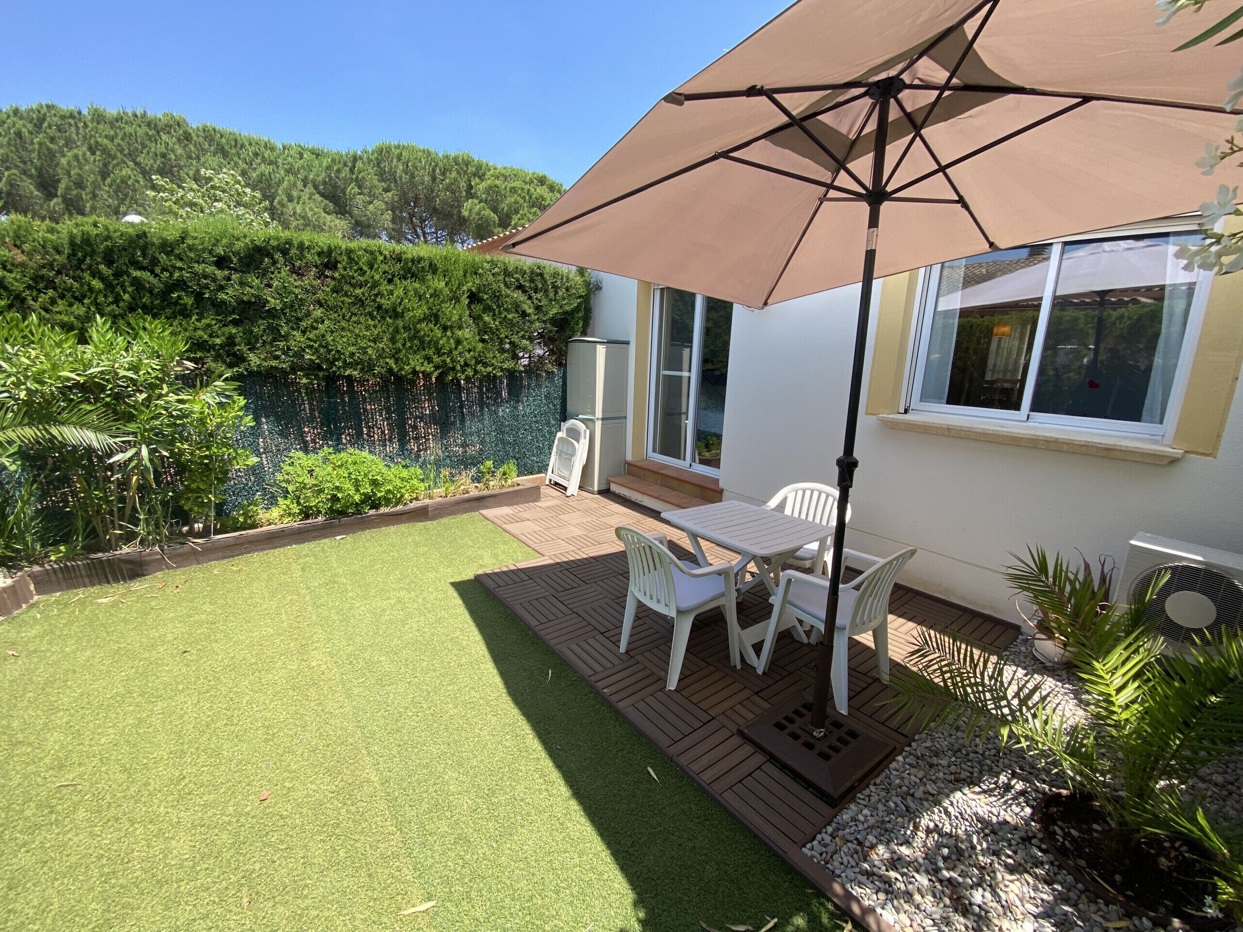 Een terras met een tafel en stoelen, een grote parasol, en een wit gebouw met een raam.