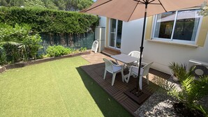 Eine Terrasse mit Tisch und Stühlen, einem großen Sonnenschirm und einem weißen Gebäude mit einem Fenster.