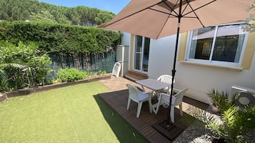 Een terras met een tafel en stoelen, een grote parasol, en een wit gebouw met een raam.