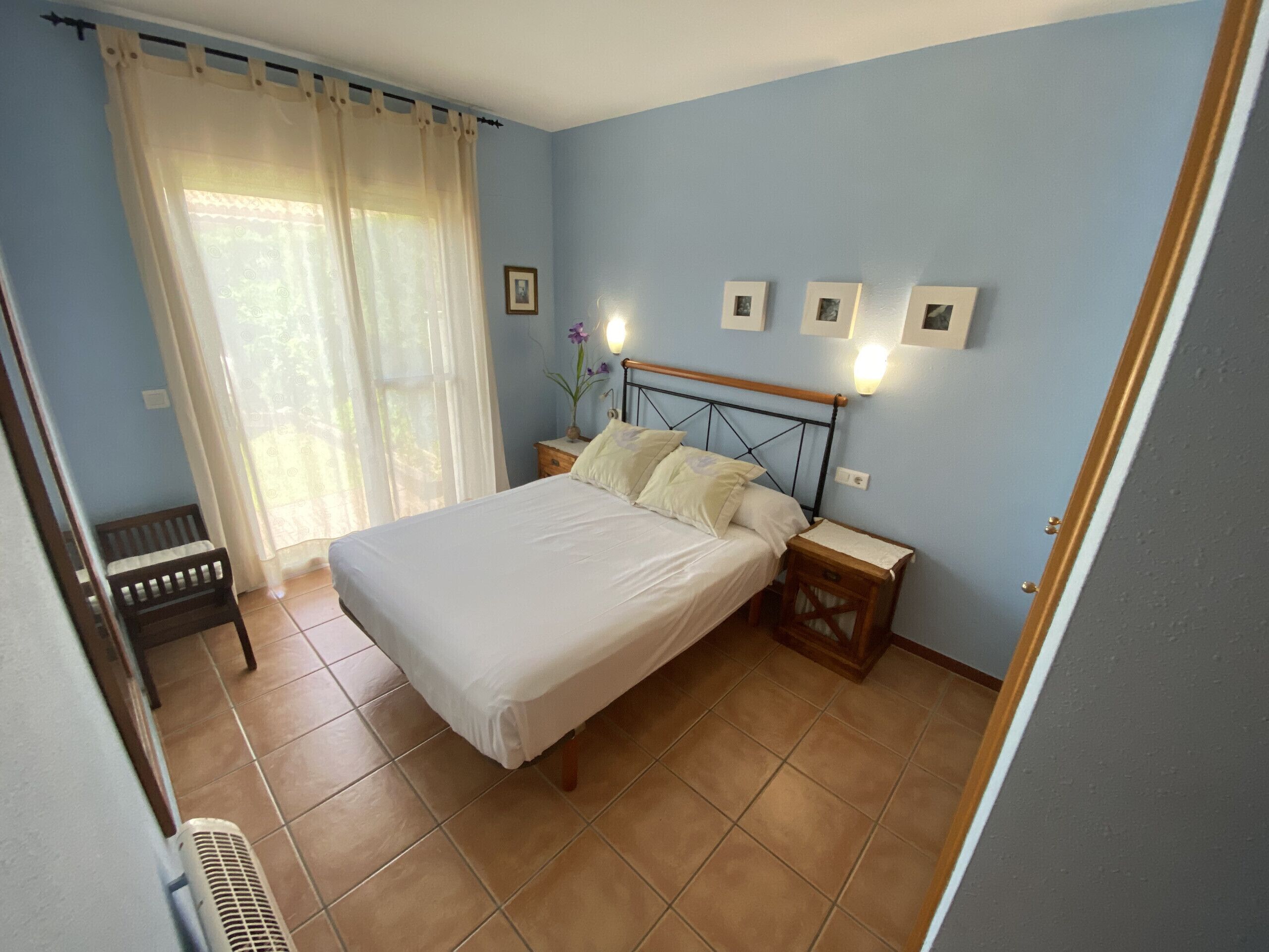 Een slaapkamer met een bed, nachtkastjes, een stoel en een raam met gordijnen.