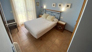 Ein Schlafzimmer mit einem Bett, Nachttischen, einem Sessel und einem Fenster mit Vorhängen.