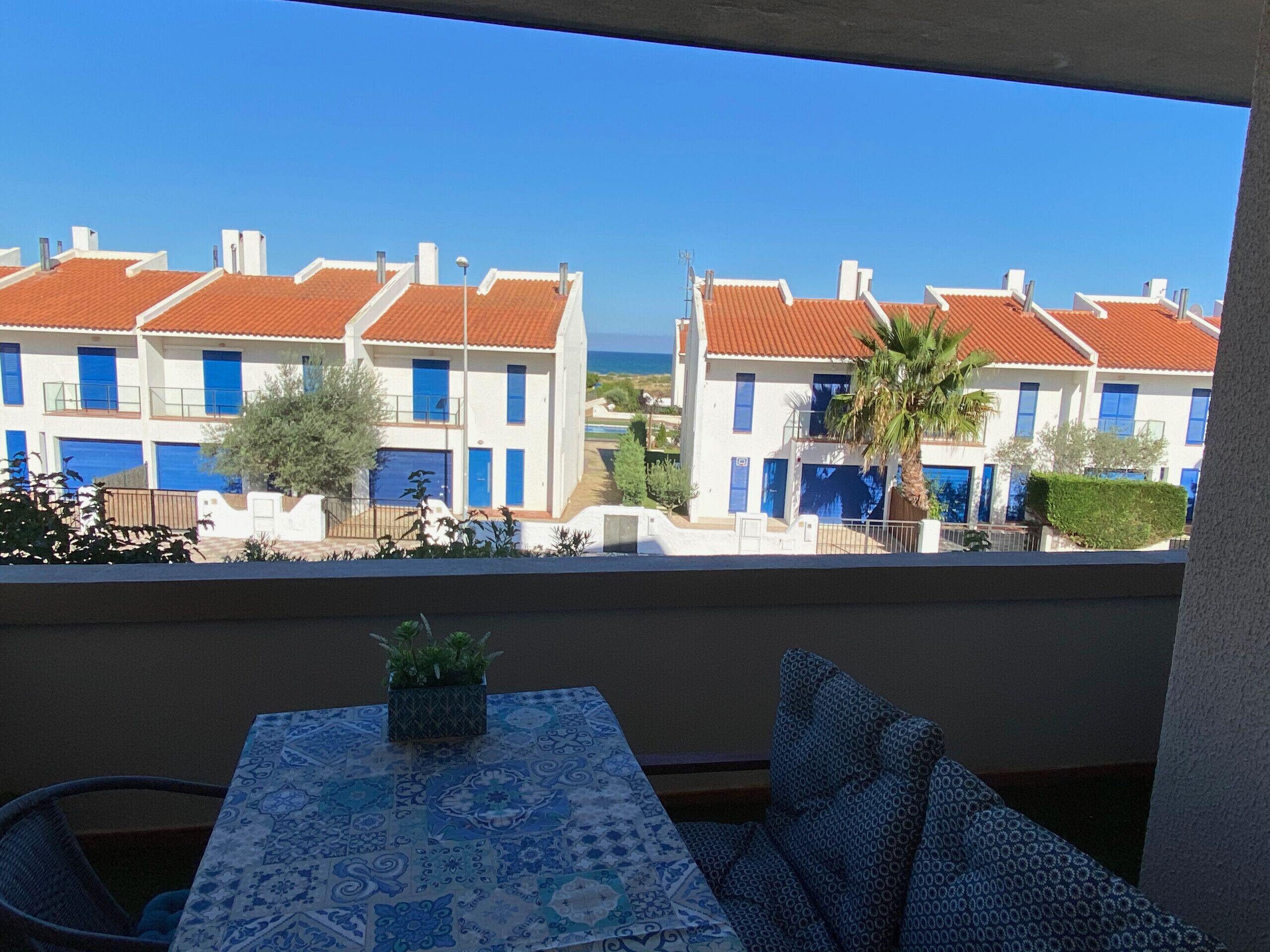 Ein Balkon mit Tisch und Stühlen, mit Blick auf eine Reihe weißer Häuser mit roten Dächern und blauen Türen.