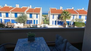 A balcony with a table and chairs, overlooking a row of white buildings with red roofs and blue doors.