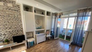 A modern living room with a brick wall, wooden flooring, a TV, a small table, and a sliding glass door leading to an outdoor area.
