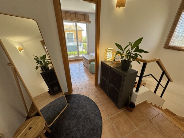 A staircase with a dark carpet, a wooden handrail, a potted plant, and a wall-mounted lamp.