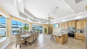 Una cocina amplia con una isla grande, electrodomésticos modernos y ventanas grandes con vistas a un puente y palmeras.