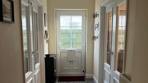 Un pasillo con una puerta que da a una habitación, un termostato y un teléfono en la pared.