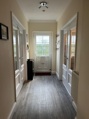 A hallway with a door leading to a room, a thermostat, and a phone on the wall.