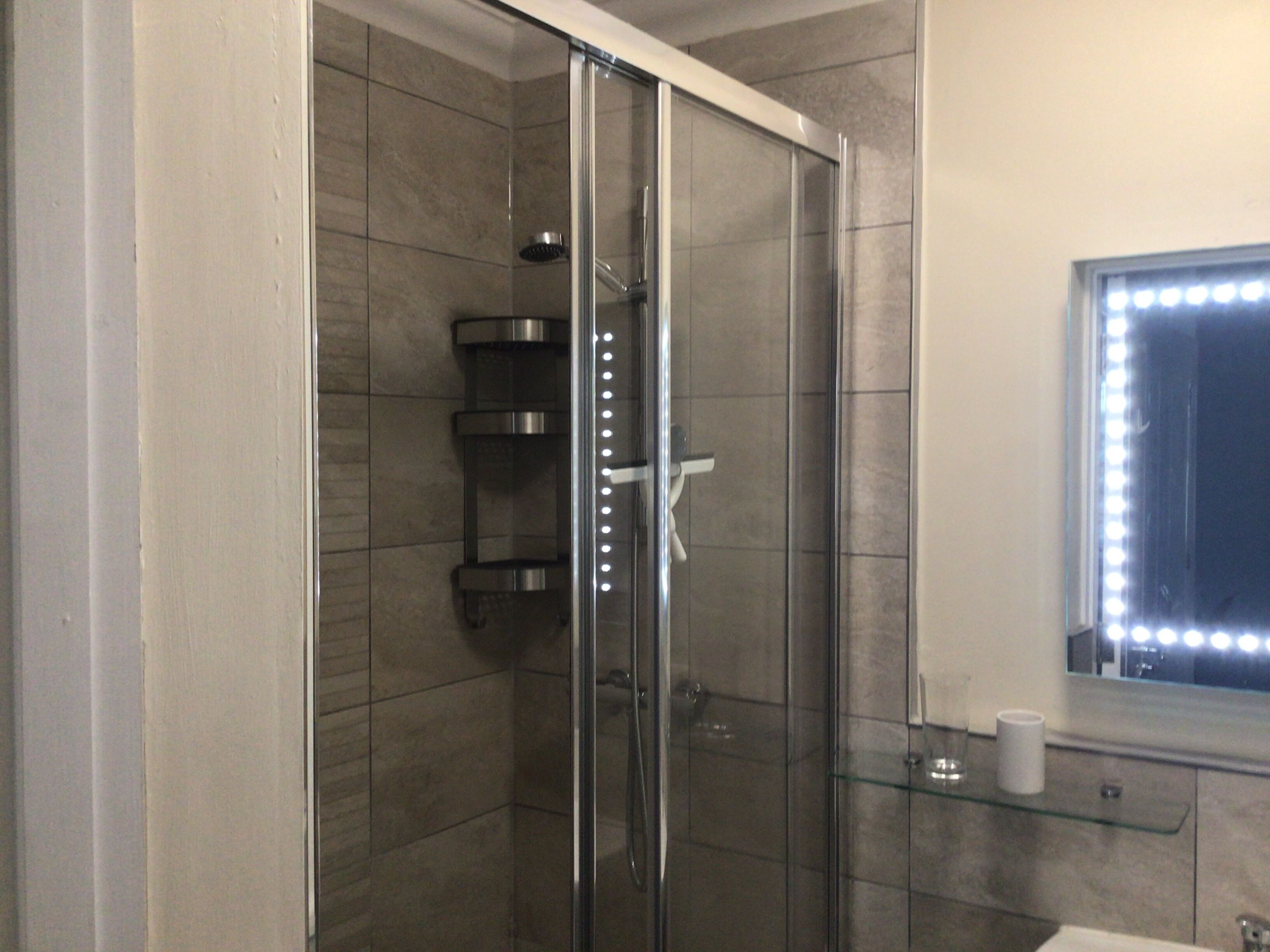 A modern bathroom with a glass-enclosed shower, a vanity with a mirror, and a glass shelf.