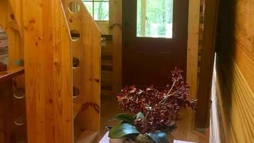 A wooden interior with a staircase, a door leading outside, and a vintage-style table with a vase of flowers.