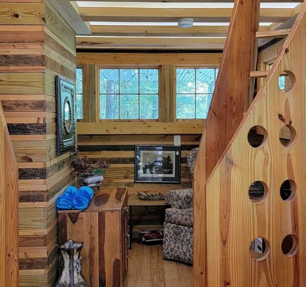 L’intérieur chaleureux d’un chalet, avec des murs en bois, un petit coin salon et une fenêtre donnant sur la verdure.