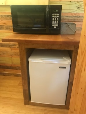 Una cuina compacta amb microones i un frigorífic petit integrat en un armari de fusta.