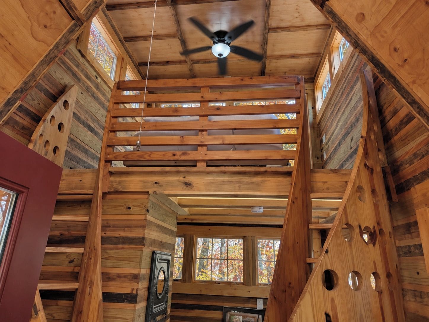 A wooden interior with a sloped ceiling, a ceiling fan, and a window with a stained glass view.