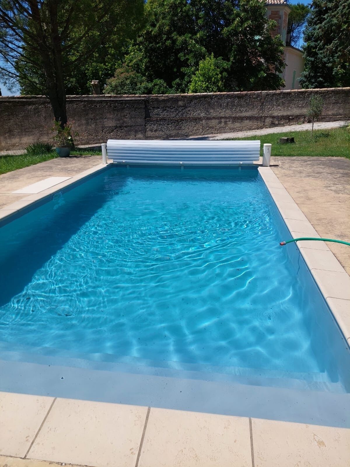 Una piscina rectangular con agua azul cristalina, rodeada por un muro de piedra y una zona ajardinada.