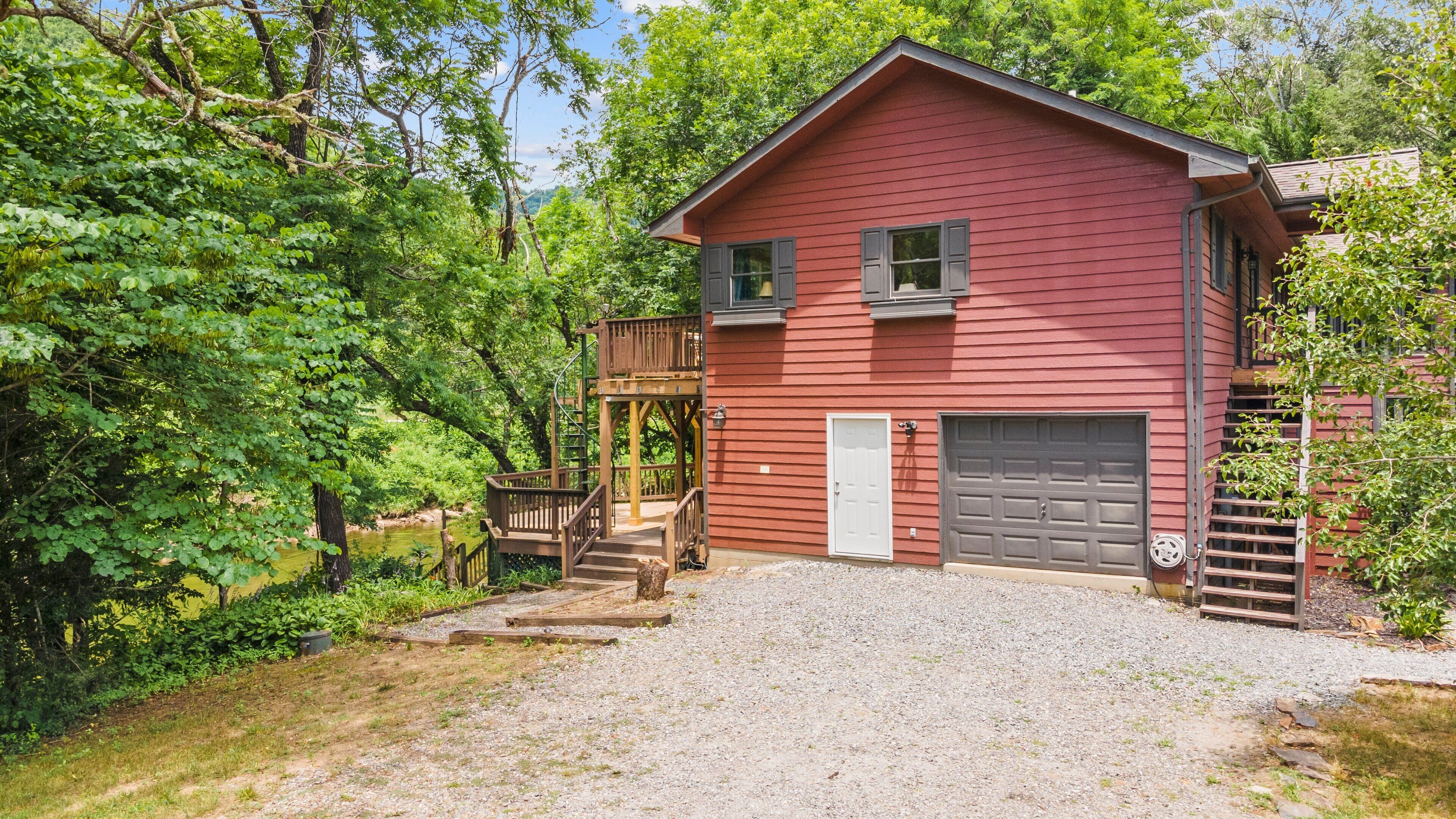 A red two-story house with a gravel driveway, a wooden deck, and a garage.