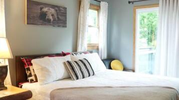 Een slaapkamer met een groot bed, een nachtkastje, een lamp, een raam met gordijnen en een plafondventilator.