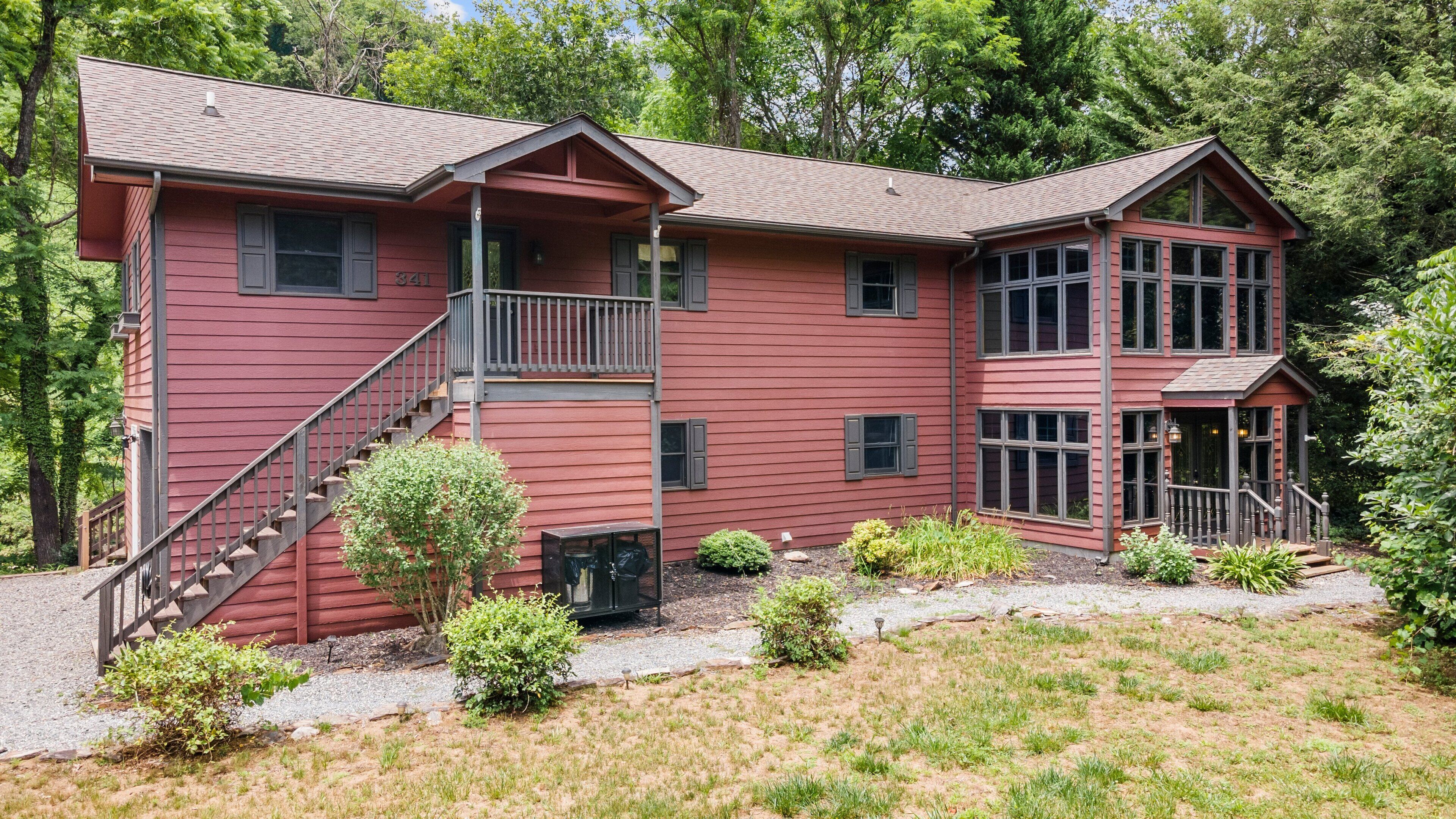 A two-story red wooden house with a balcony, a covered porch, and a gravel driveway.