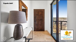Un couloir avec une lampe, une porte en bois et une vue sur un balcon doté d’une rambarde en métal.