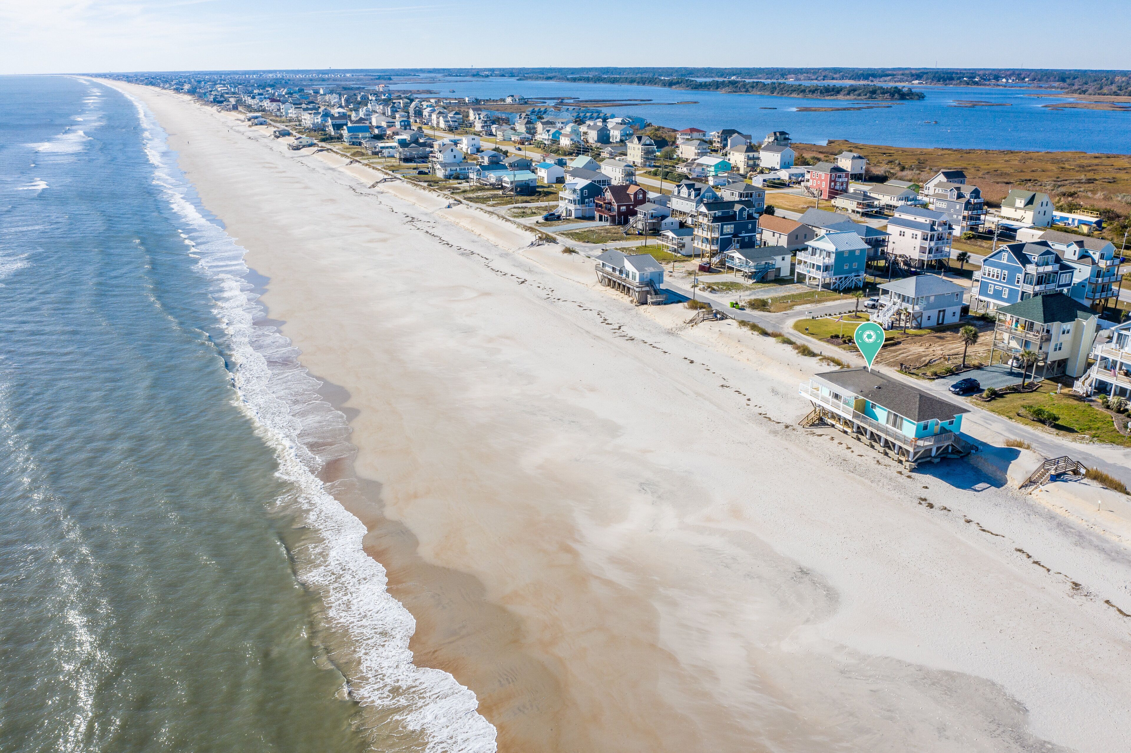 An aerial view of a coastal residential area with houses along the beach and a body of water in the background.