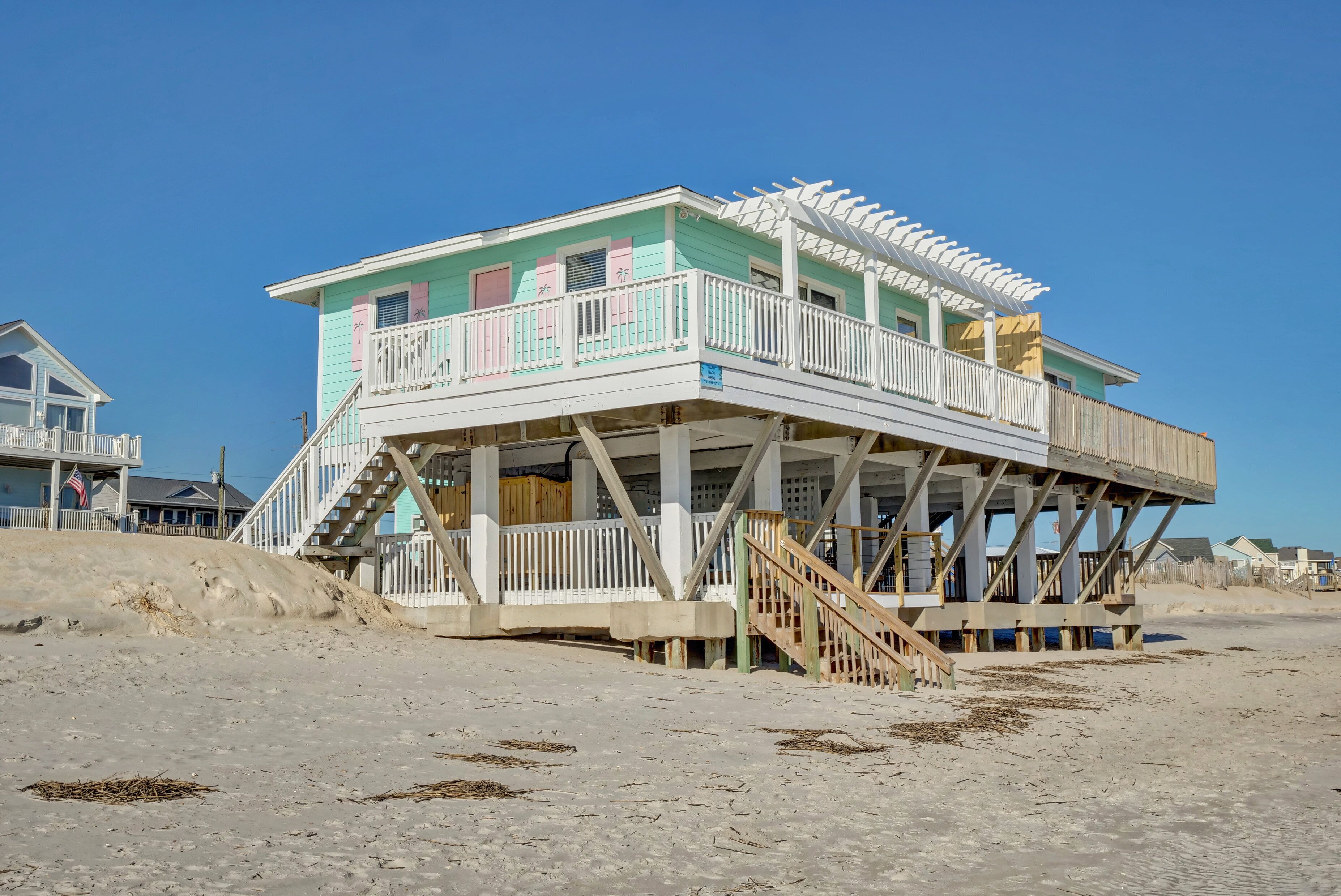 Une maison située en bord de mer, dotée d’un balcon, d’une terrasse en bois et d’un escalier menant à l’entrée.
