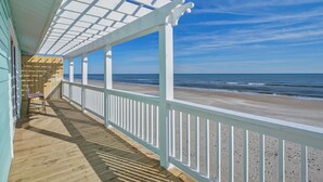 Eine Holzterrasse mit weißer Reling, die auf einen Strand blickt.