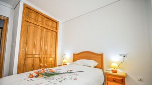 Et soveværelse med et træskab, en seng med blomstret sengetæppe, to sengeborde og et natbord med lampe.