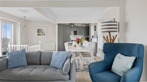 Ein modernes Wohnzimmer mit grauem Sofa, einem blauen Sessel und einem Essbereich mit weißem Tisch und Stühlen.