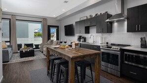 Una cocina moderna con una isla central, taburetes de bar, electrodomésticos de acero inoxidable y un comedor con sofá y sillas.