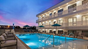 Un hotel moderno con piscina en la azotea, tumbonas y sombrillas.