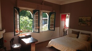 Een slaapkamer met een bed, een bureau en een raam met open luiken.
