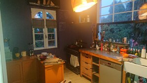 Een keuken met een fornuis, oven, en diverse keukenspullen op het aanrecht. Er is een raam met uitzicht op bomen.