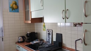 Een keuken met witte kastjes, een zwarte waterkoker, een wijnglas en een snijplank met een tomaat en kaas etiket.