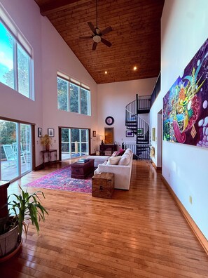 Un vaste espace de vie doté d’un plafond en bois, de grandes fenêtres, d’un escalier et d’une peinture abstraite aux couleurs vives.
