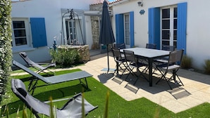 Een terras met een tafel, stoelen, een schommelset en een kleine tuin.