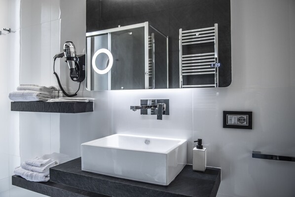 A modern bathroom with a large rectangular sink, a hairdryer on a wall-mounted shelf, and a towel rack.