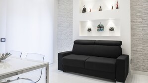 Una sala de estar moderna con un sofá negro, una mesa de comedor de vidrio y una pared de ladrillo blanco.