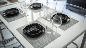 Una mesa de comedor dispuesta con platos negros, copas transparentes y una copa de vino, con un diseño moderno y minimalista.