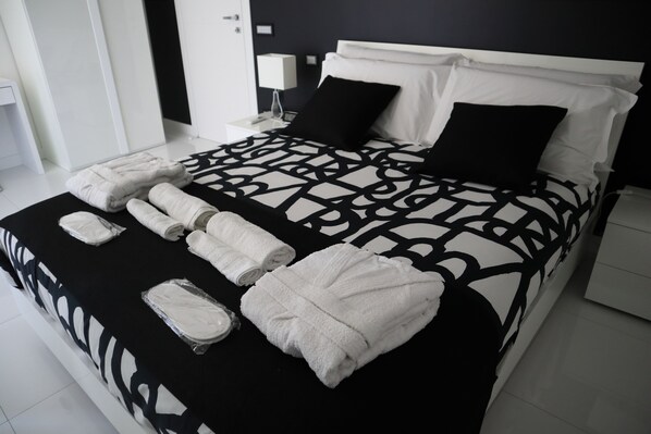 A neatly made bed with a patterned bedspread, two black pillows, and several rolled white towels.