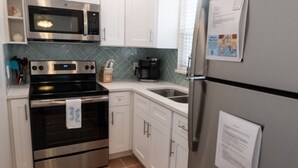 A compact kitchen with white cabinets, stainless steel appliances, and a tiled backsplash. - LOCATION!! Cabana just steps from the beach! (Holmes Beach)