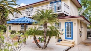 A two-story building with a balcony, a blue door, and a small garden with palm trees. - LOCATION!! Cabana just steps from the beach! (Holmes Beach)