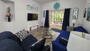 Un salon moderne avec une table basse en verre, des canapés bleu foncé, un téléviseur à écran plat et une vue sur l’extérieur grâce à une porte vitr ée.