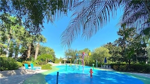 Une piscine avec un toboggan, entourée d’arbres et bordée d’un chemin en briques.