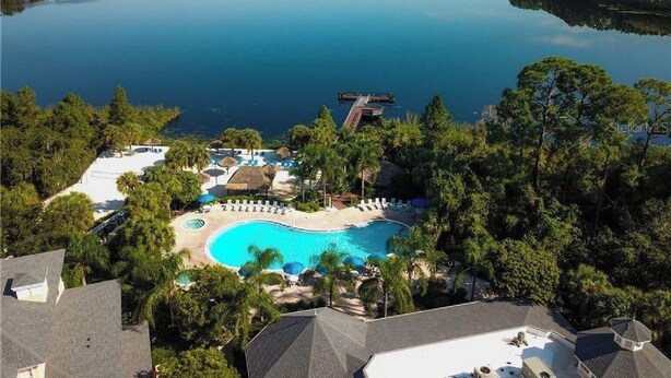 Un complexe hôtelier doté d’une grande piscine entourée de palmiers et d’une jetée s’avançant dans un lac paisible.