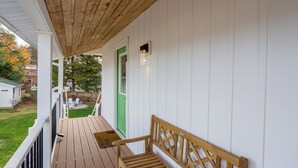 Um deck de madeira com um banco, uma porta verde e uma parede externa branca.